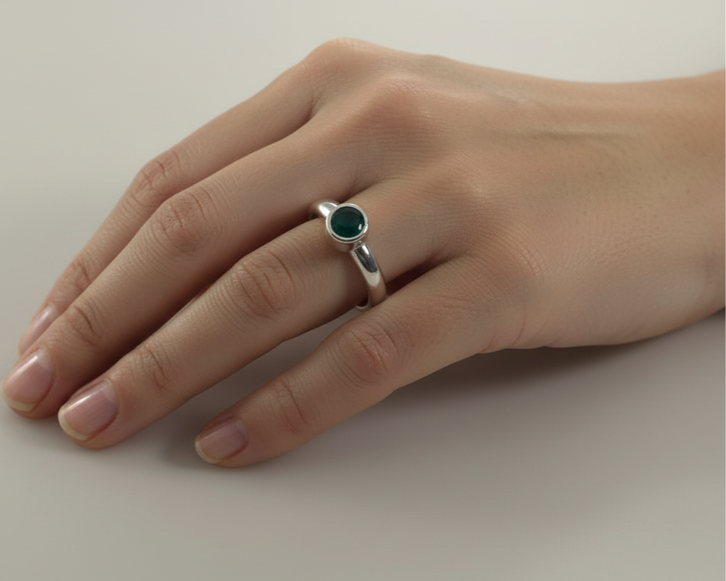 Silver ring with a green resin in a collet on a hand against a neutral background