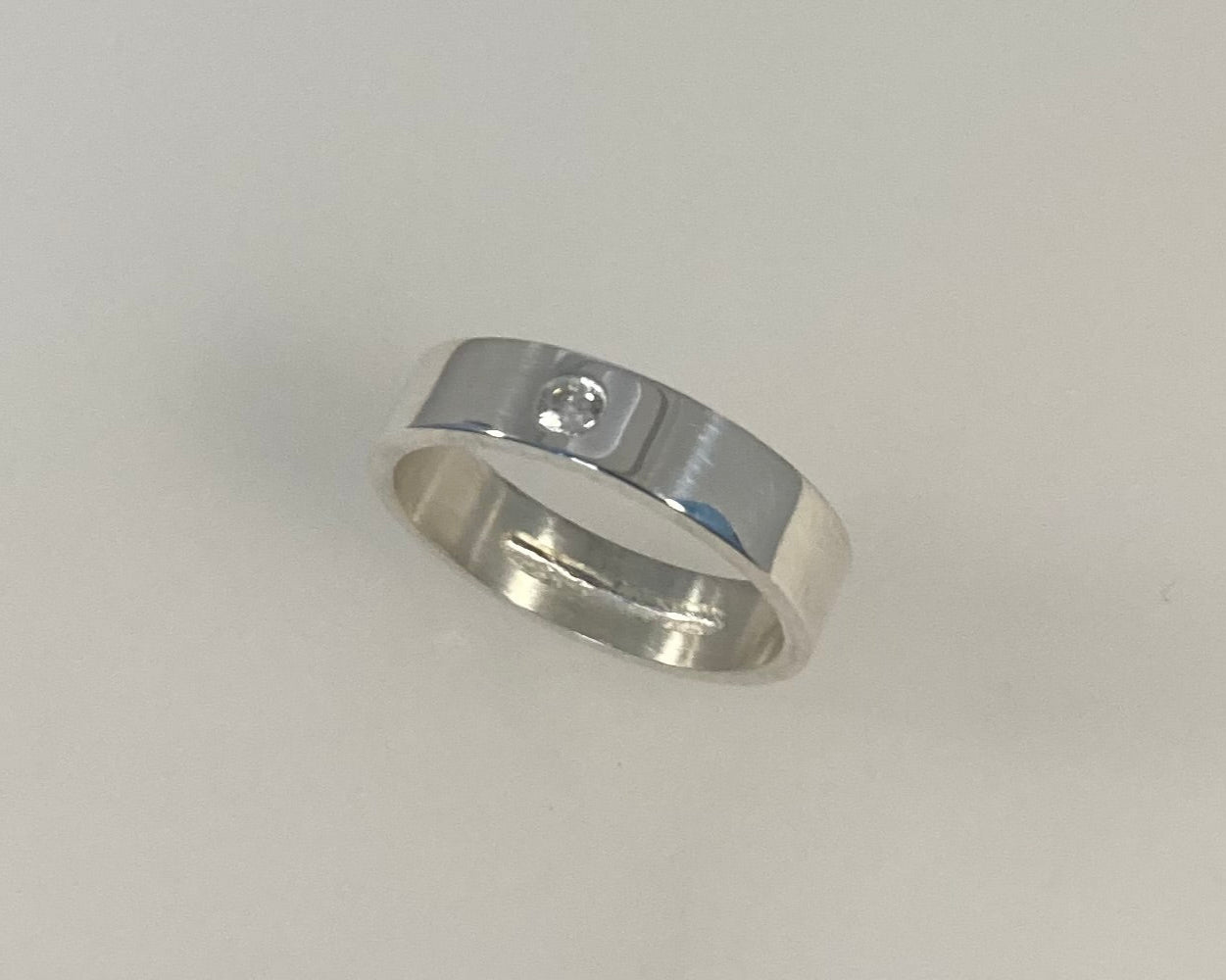 Single Brilliant cut stone set in rub over 5mm wide flat ring with hidden ashes inside shank